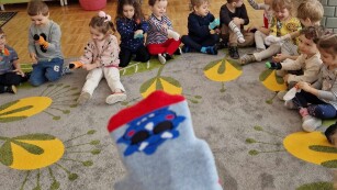dzieci siedzą na dywanie, na ręce mają założone skarpetki